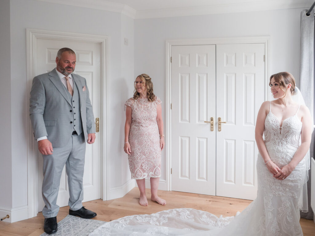 Bride smiles at her father, who is seeing her wedding dress for the first time