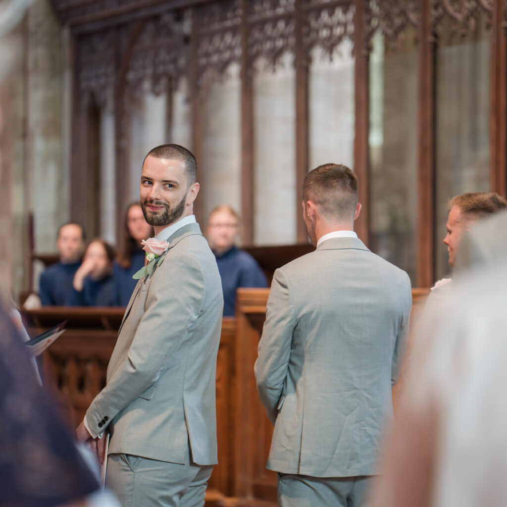 Groom looks over his shoulder at his bride in Romsey Abbey
