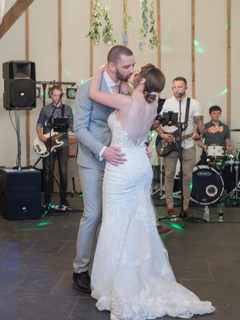 Bride and groom kiss on the dance floor as a rock band plays in the background at Kimbridge Barn
