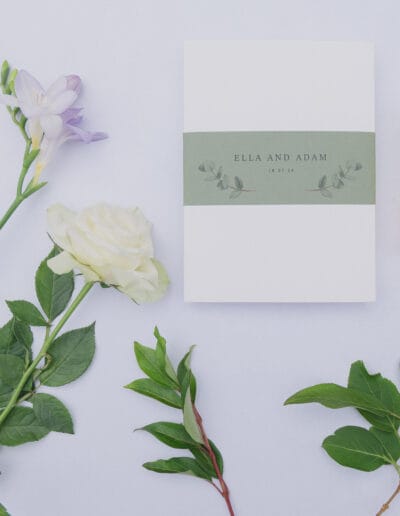 Flat lay of wedding stationery, l'Occitane perfume bottle and flowers
