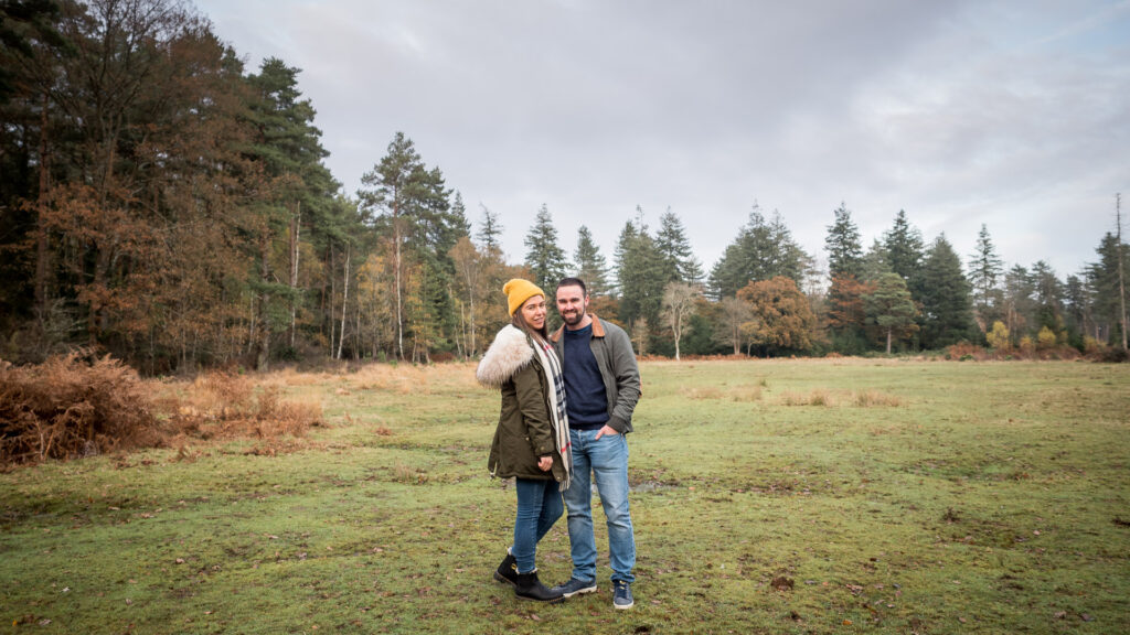 Couple stand in a woodland clearing, smiling, in autumn