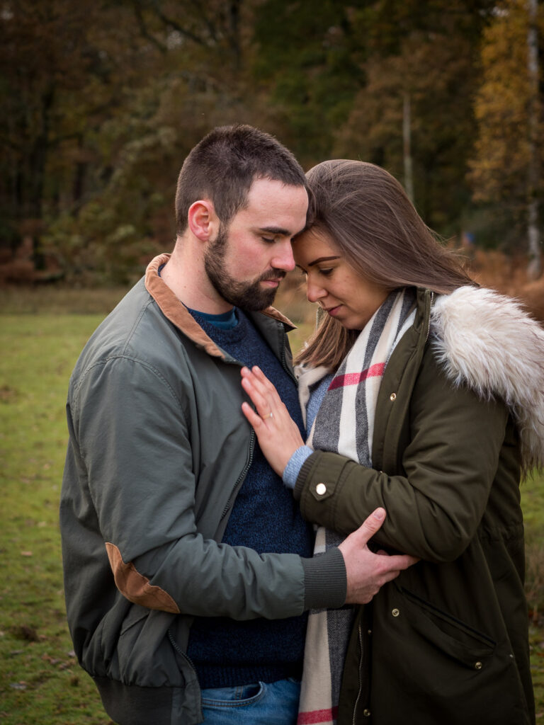 Couple stand quietly, heads together, the woman with her hand on her fiancé's chest