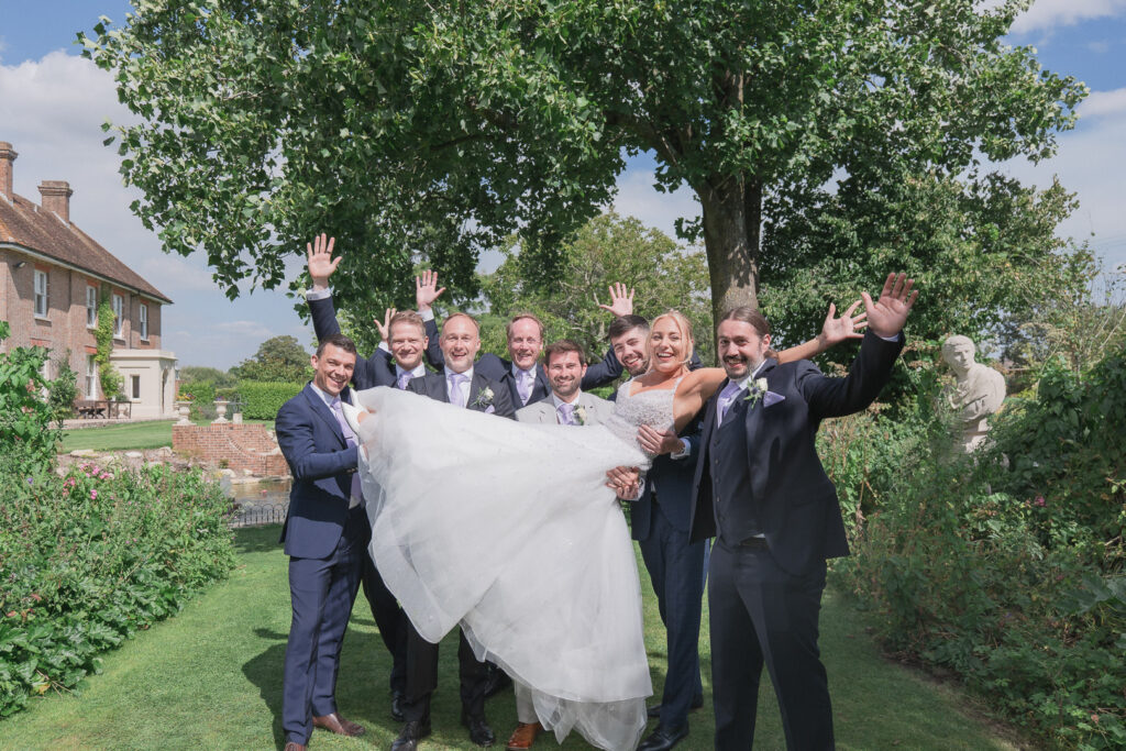 Groomsmen wave as they hold bride aloft at Parley Manor
