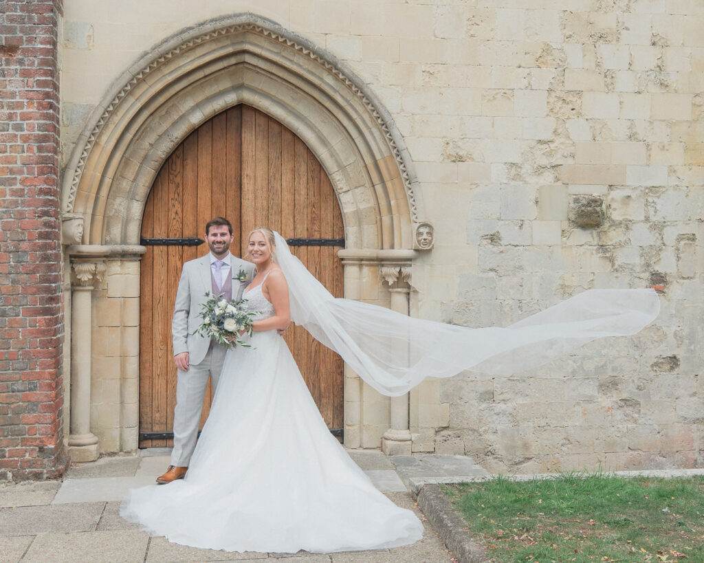 Veil billows out from bride with her groom outside Romsey Abbey