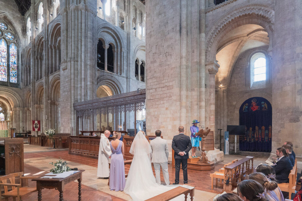 Woman reads lesson during wedding in Romsey Abbey as bride and groom look on