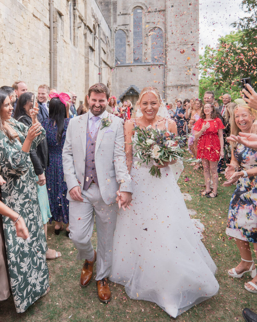 Guests shower bride and groom with confetti outside Romsey Abbey
